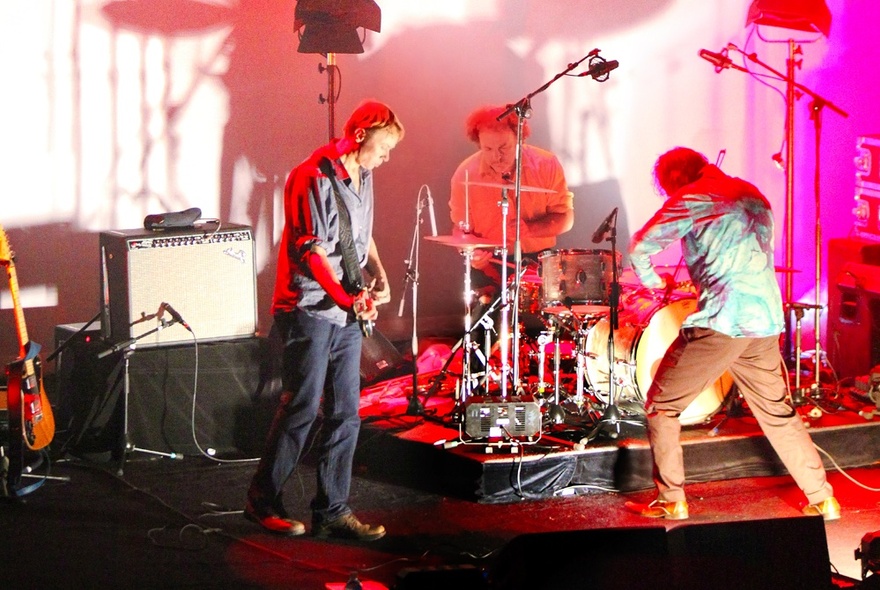 The three-piece band, The Dirty Three, performing with their instruments on a small stage.