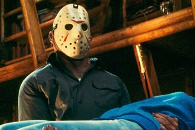 A movie still showing a masked man carrying a body.