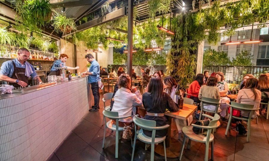 A busy rooftop bar with plants hanging from the ceiling.