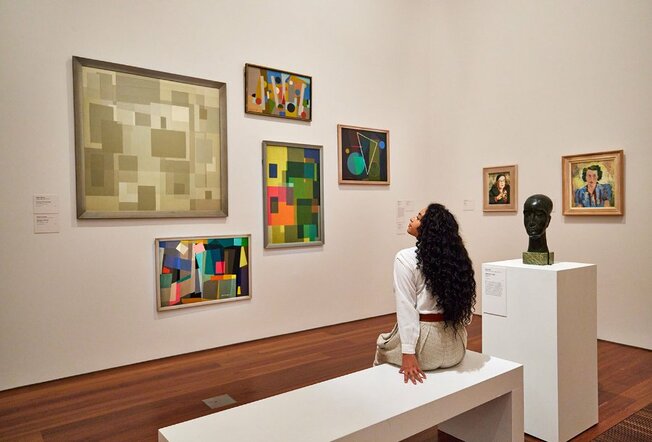 A woman sitting on a bench and looking at paintings in an art gallery. 