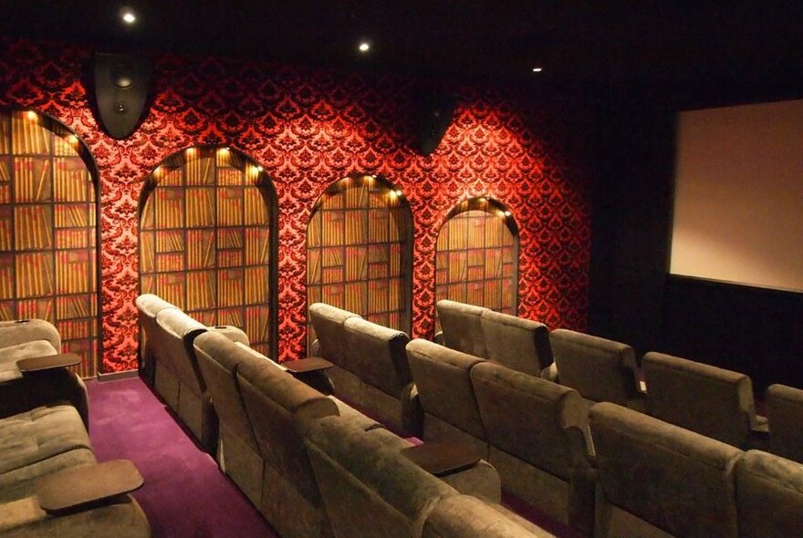 Rows of comfortable chairs in a cinema, with decorated walls, soft down lights and the edge of a cinema screen visible.