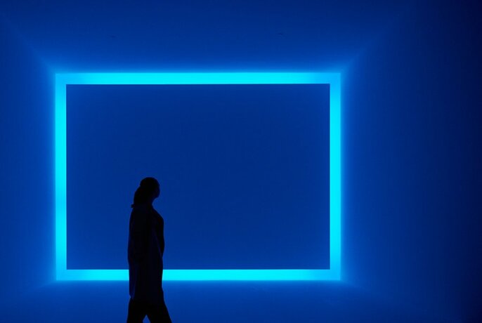 A woman walking past a glowing blue square art exhibit.