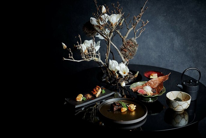 Elegant dishes surrounding a twig floral centrepiece on a black table against grey walls.
