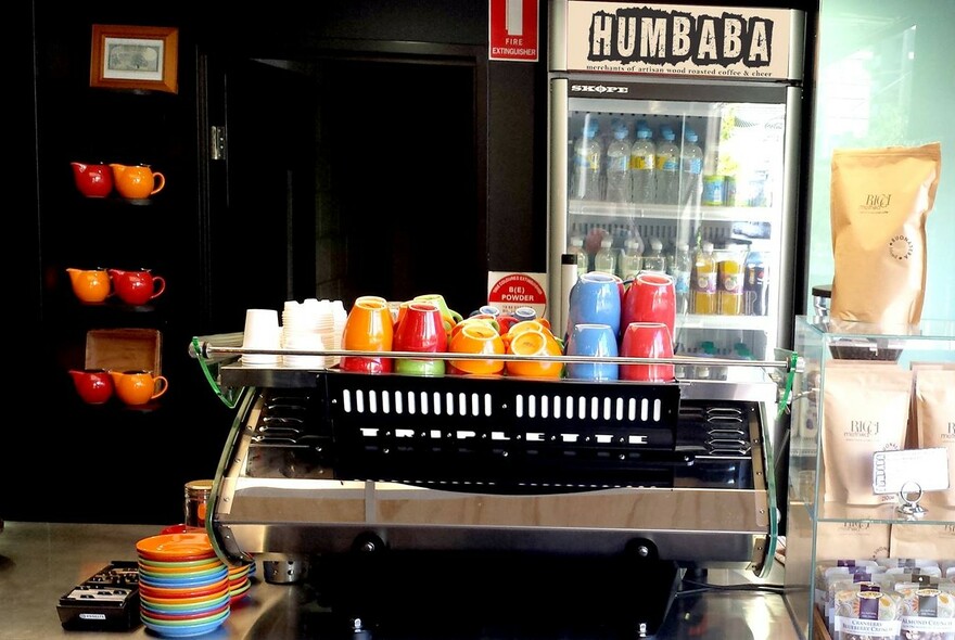 Coffee machine with colourful cups atop and fridge with the word Humbaba up top, at rear.