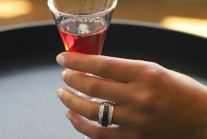 Woman's hand holding a small glass of red-coloured drink and wearing a diamond ring.