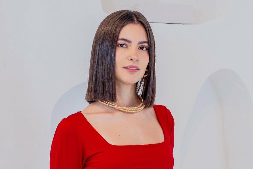 A model with straight brown hair, a gold necklace modelling a red square necked top.