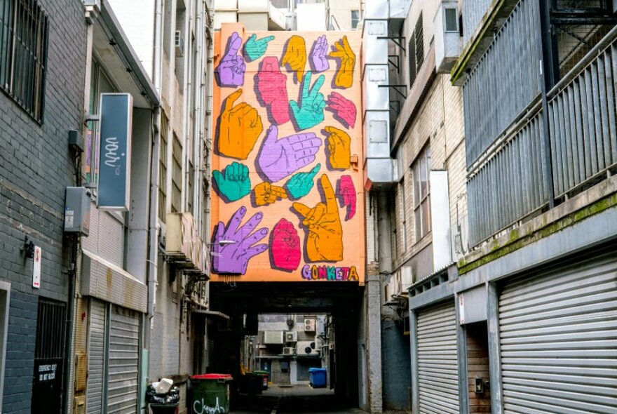 A large colourful mural with hand signs on a wall at the end of an alleyway.