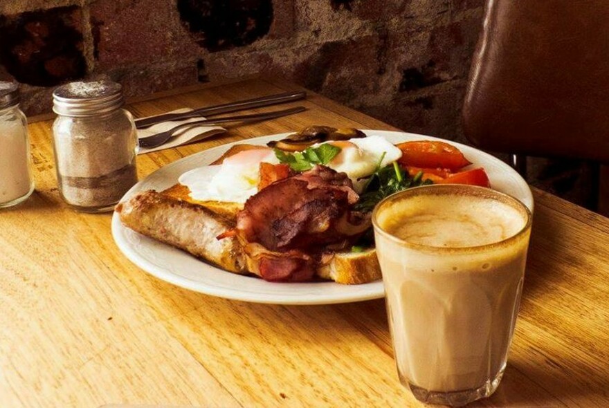 Coffee next to a plate of eggs and bacon.
