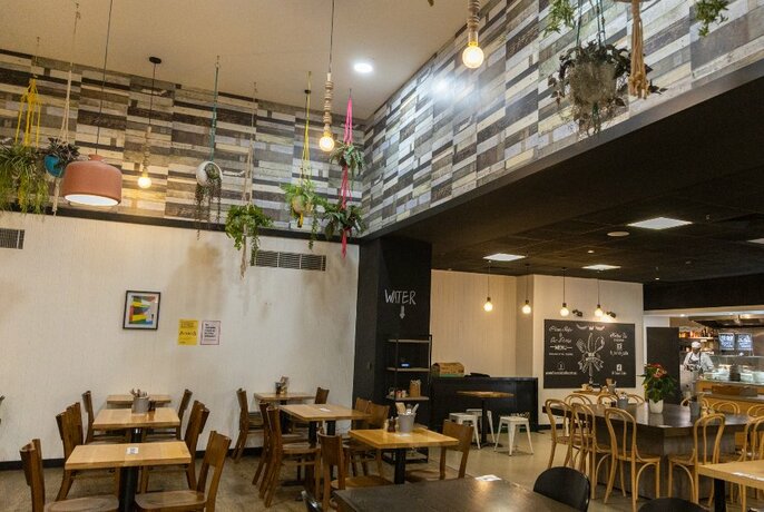 A cafe with lots of dining tables and hanging plants