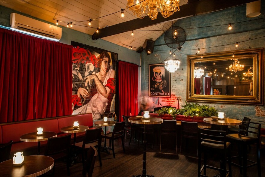 Interior of Murmur featuring wooden floor, red curtains, small candlelit tables and banquette seating.