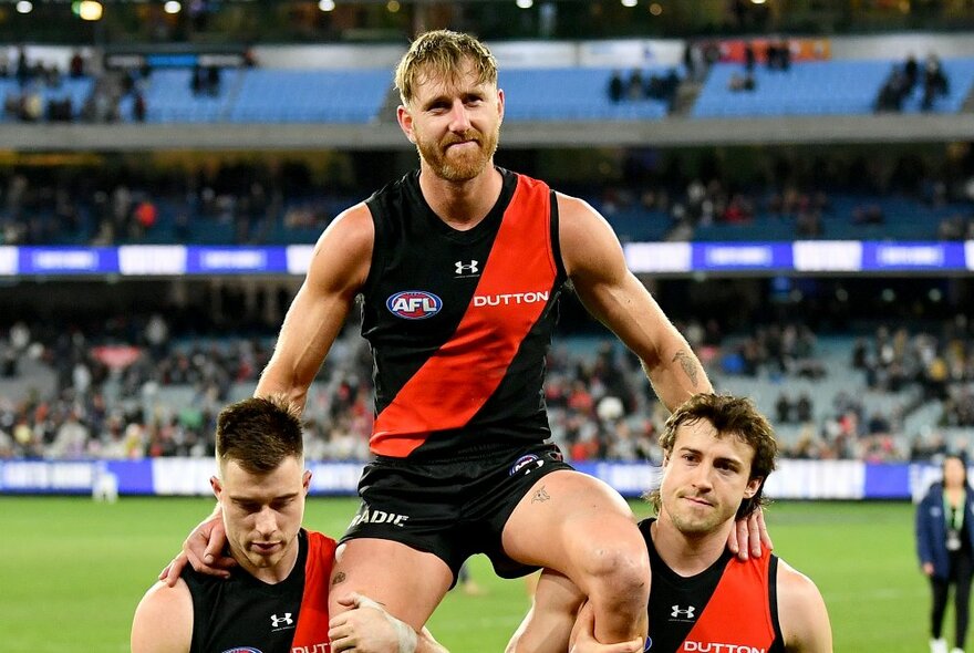Two Essendon AFL football players carrying a third on their shoulders after a game.