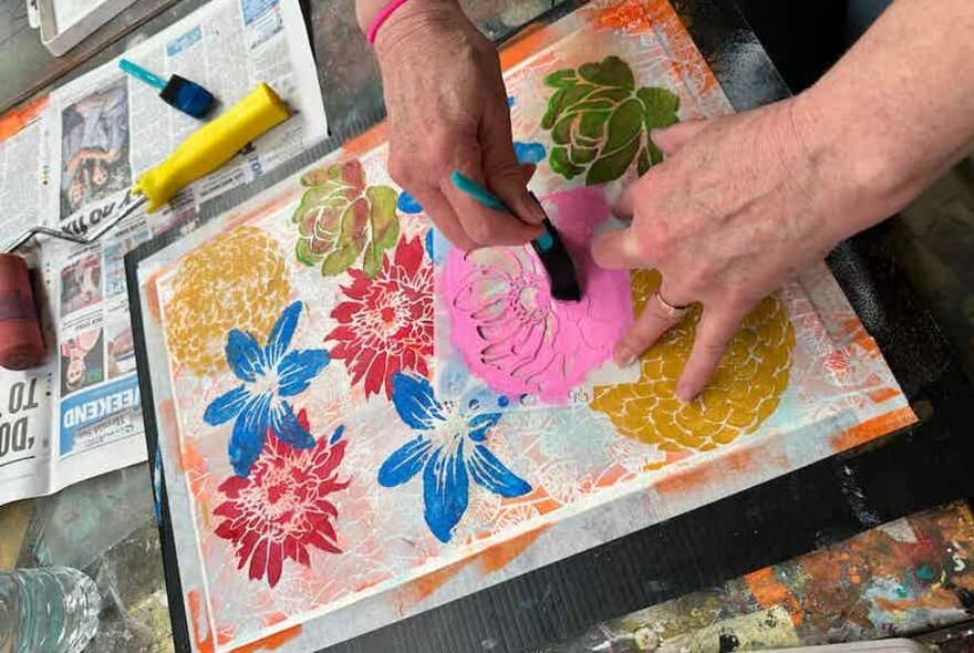 Looking down on a person creating colourful stencil flowers on fabric.
