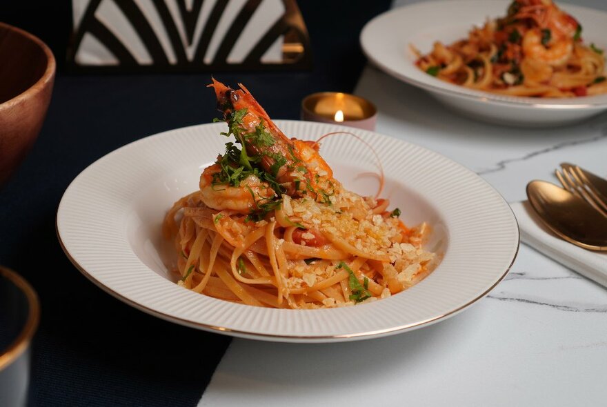 A table with a bowl of spaghetti with a King Prawn on top. 