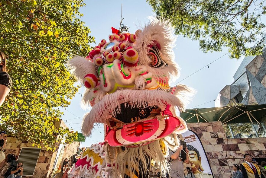 A lion dancer in a colourful costume on a sunny day in the city.