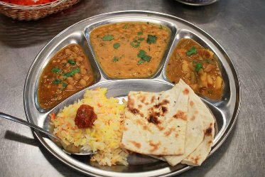 Indian thali meal with three curries, rice and naan bread.