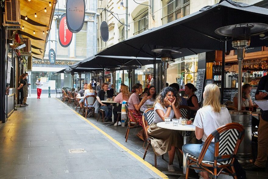A busy laneway with people dining at outdoor tables.