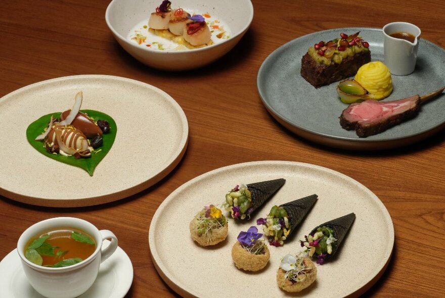 Several dishes of carefully arranged restaurant-styled food on ceramic plates and bowls on a  wooden table.