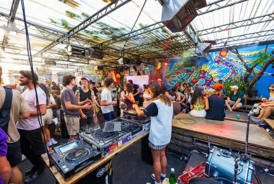 A DJ performing in an art-filled outdoor bar.