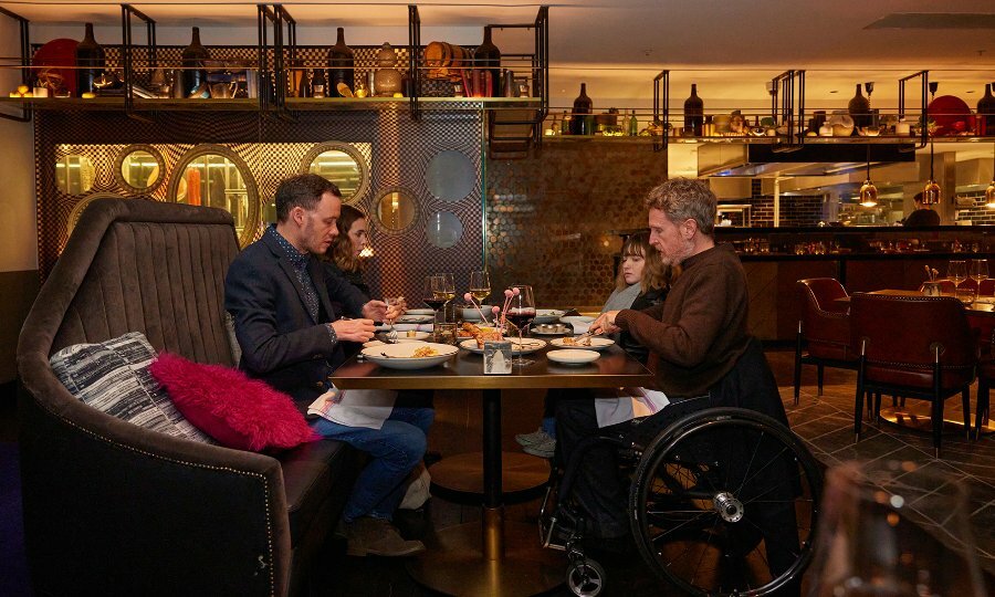 Four diners eating in a restaurant, two are sitting in wheelchairs.