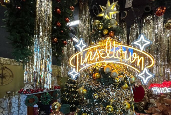 A room decorated with a large Christmas tree with the words 'Tinseltown' in neon lights displayed in front of it.