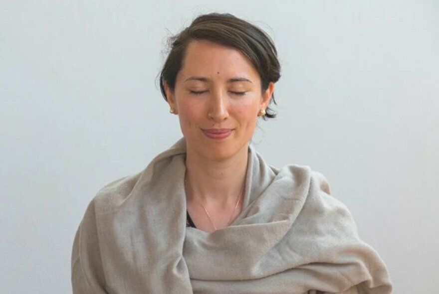 Woman with eyes closed, calm look on face, wrapped in a beige shawl.
