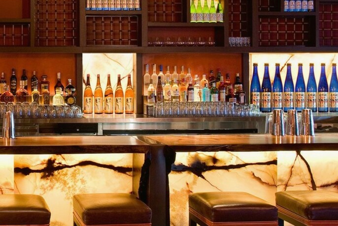 Nobu's backlit marble bar with stools and shelves filled with bottles and glasses.