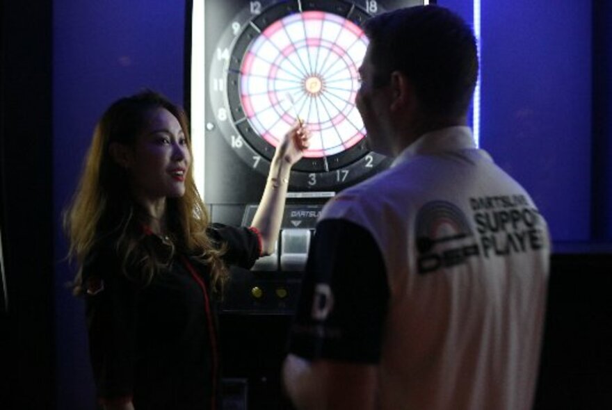 People standing in front of a backlit electronic darts board.
