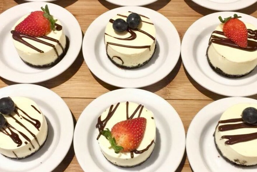Row of white plates with round cream desserts drizzled with chocolate and strawberries.