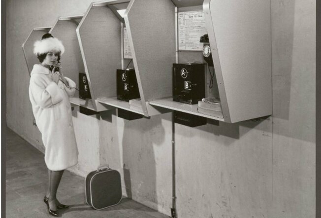 A black and white photo of a woman at a phone booth
