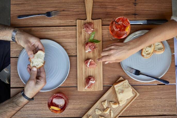 Two people enjoy a charcuterie board with bread and pastrami.