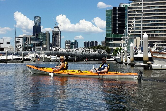 A yellow double kayak on the Yarra River with the Melbourne skyline on the background