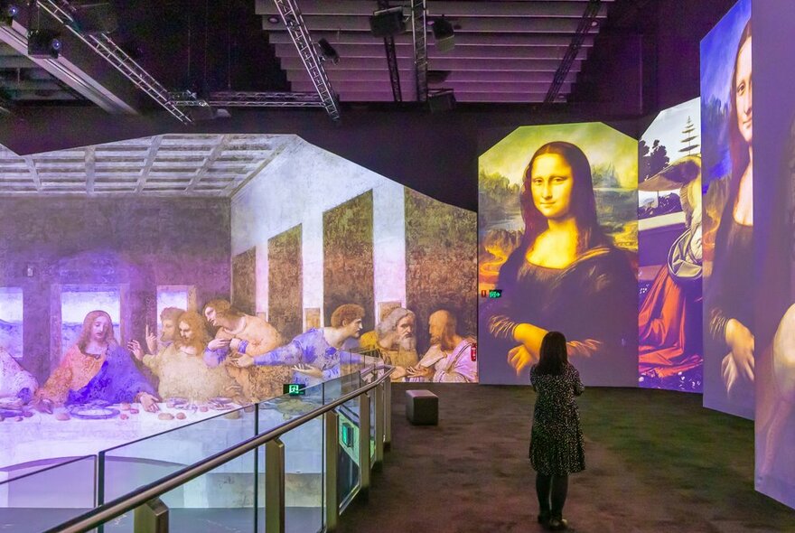 A woman is standing in a digital projection art gallery looking at a picture of the Mona Lisa