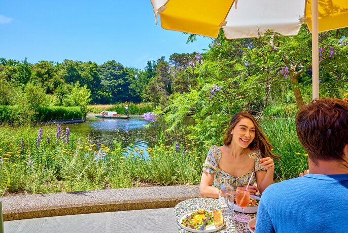 A couple sharing colourful dishes and drinking spritzes at a lakeside outdoor cafe table.