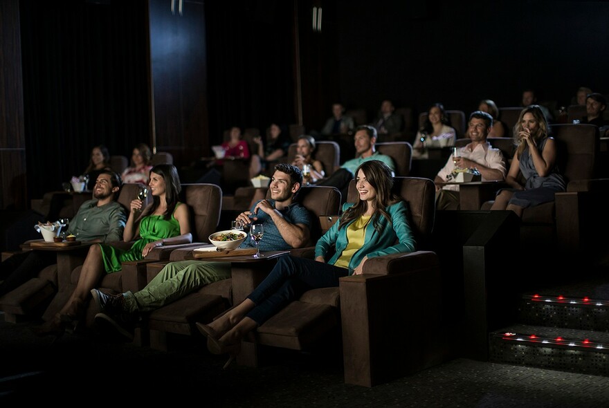 Patrons enjoying in-cinema dining and plush recliners in an intimate setting. 