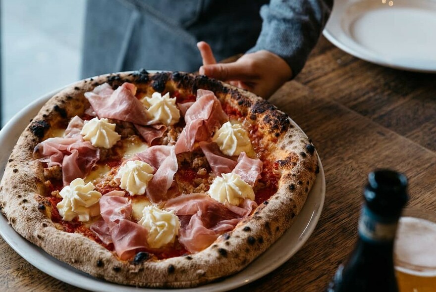 Waiter placing a prosciutto pizza on a wooden table.