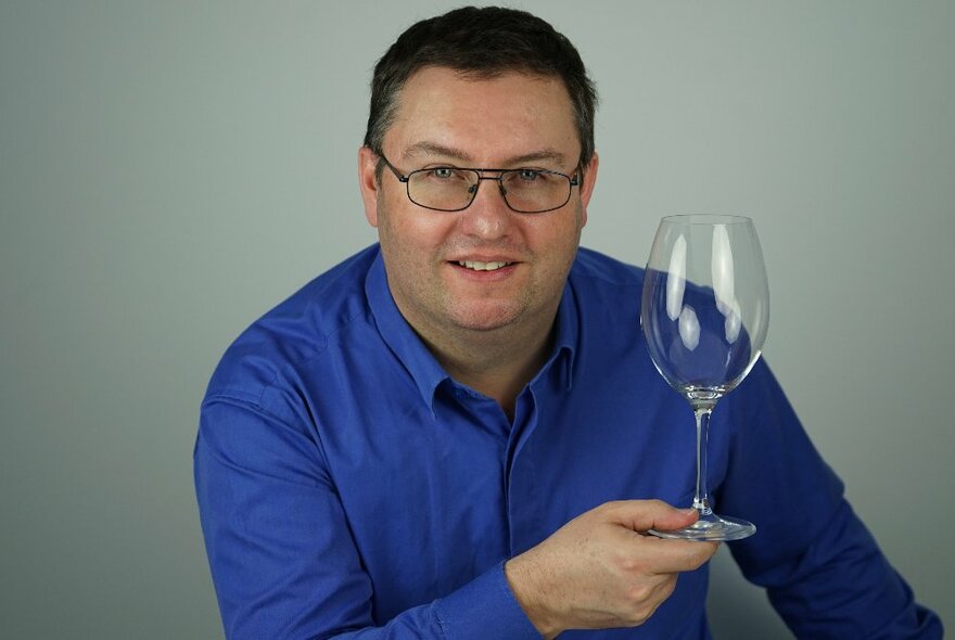 Man wearing a blue shirt and glasses, holding an empty wineglass.