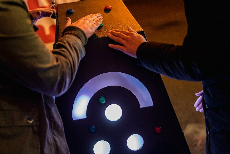 People pressing their hands on a large box with coloured buttons and lights. 