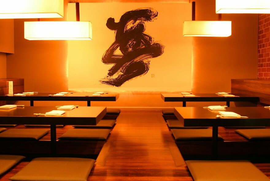 Low Japanese-style bench tables with pendant lighting and calligraphy artwork.