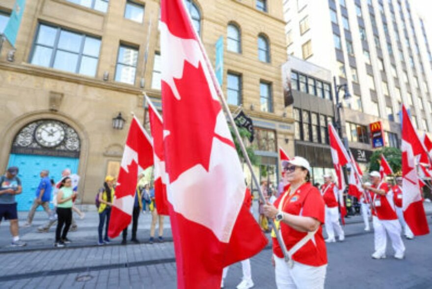 People wearing the colours of their nation, in this case Canada, carrying flags and walking in a street parade.