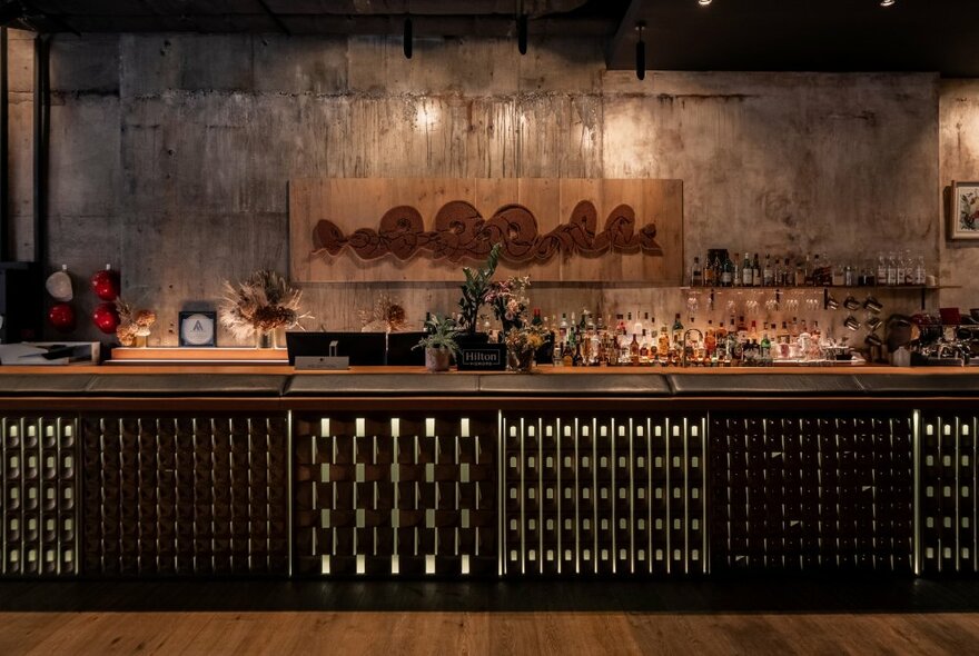 A softly lit bar in a hotel, in shades of brown and tan, with an artwork hanging in the back wall.