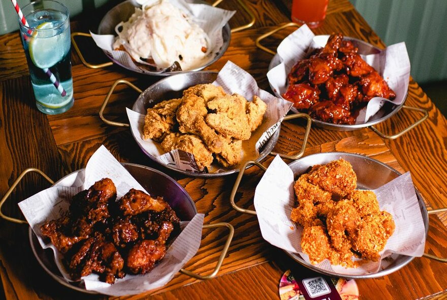 A table with plates of Korean fried chicken and a blue cocktail