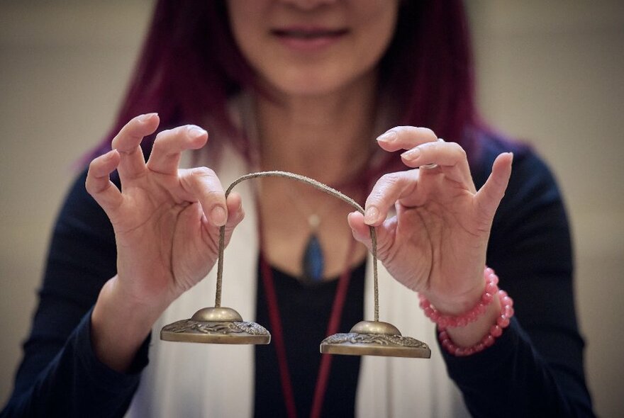 A woman holds two tiny linked brass bells in front of her. 