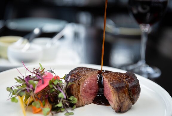 A steak sliced open through the middle to display a medium rare cook, with sauce being drizzled over it. 