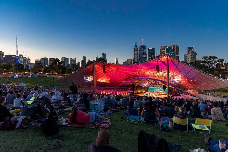 Audience seated on the grass at the Sidney Myer Music Bowl in Melbourne at dusk.