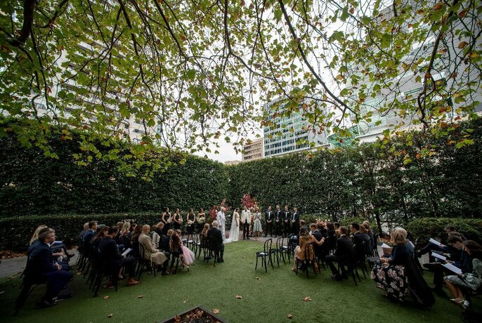 Wedding party and guests (seated) in garden settings with buildings in background.