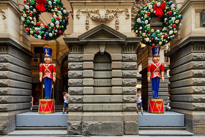 Two giant tin soldiers decorating the entrance to Melbourne Town Hall, standing underneath Christmas wreaths.