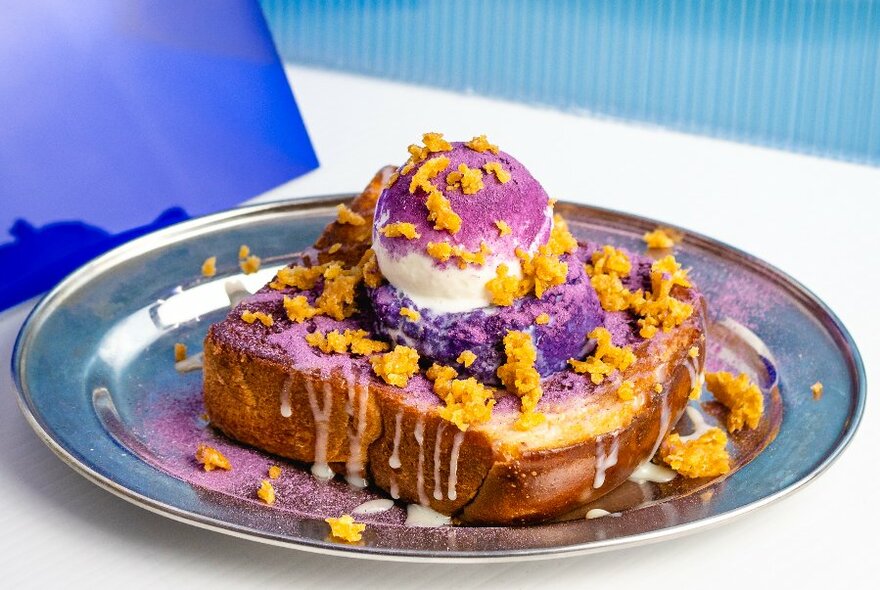 A purple dessert showing a thick slab of brioche with ice cream and sauces.