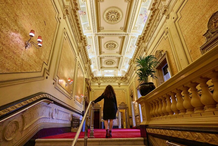 A woman walking up a staircase in a beautiful old theatre.