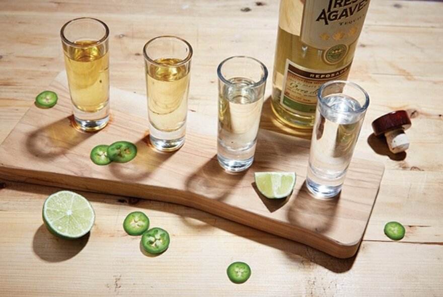 Wooden platter loaded with tequila drinks, lime and chillies.