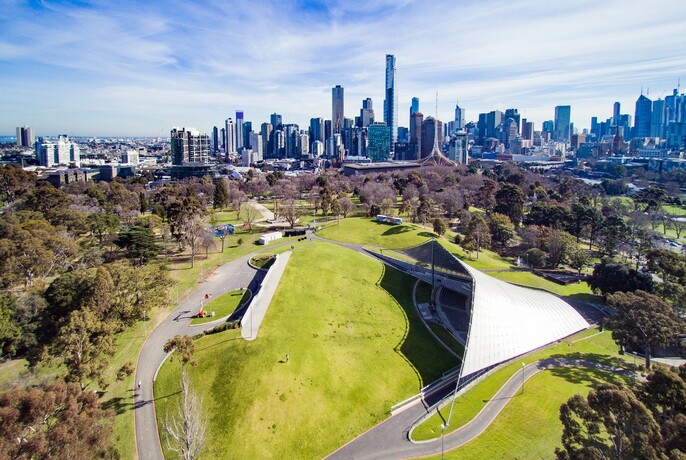 Aerialview of Sidney Myer Music Bowl showing open grassy area, covered stage and city beyond.